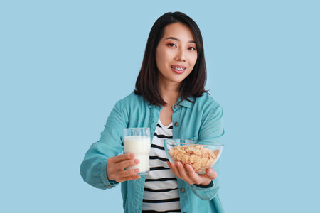 Young Asian woman with milk and cornflakes on light blue backgroundの写真素材