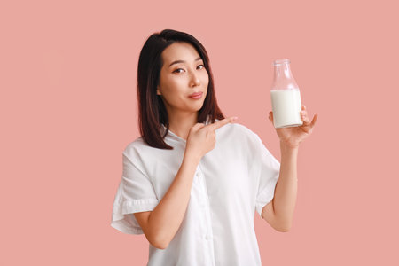 Beautiful Asian woman with bottle of milk on pink backgroundの写真素材