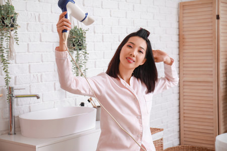 Pretty young Asian woman drying hair in bathroomの写真素材