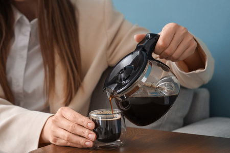 Woman pouring coffee from pot into glass on tableの写真素材