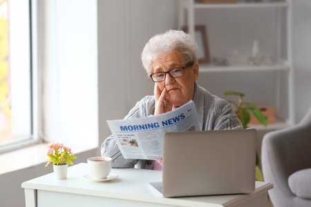 senior woman reading newspaper at homeの写真素材