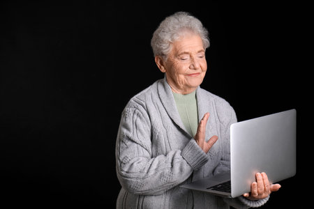 Senior woman with laptop video chatting on black backgroundの写真素材