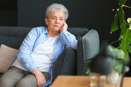 Sad senior woman sitting on sofa at homeの写真素材