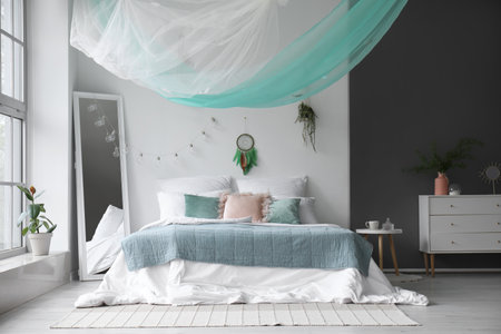 Interior of modern bedroom with bed, mirror and dream catcher hanging on light wallの写真素材