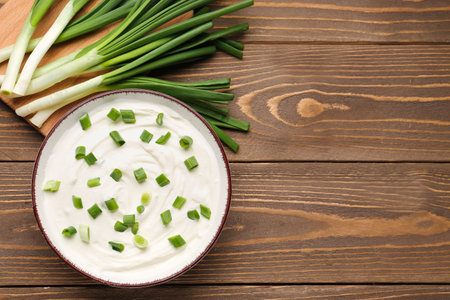 Bowl of tasty sour cream with green onion on wooden backgroundの写真素材