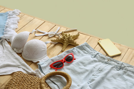 Clothes with beach accessories, starfish and mobile phone on wooden pontoon against green background. travel conceptの写真素材