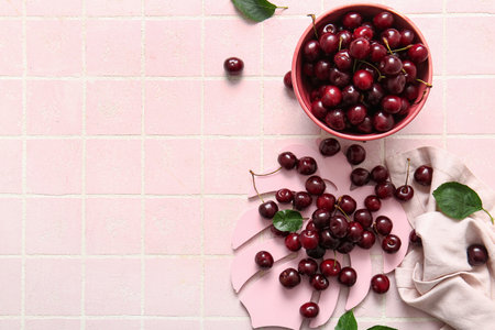 Bowl and decorative palm leaf with sweet cherry on pink tile backgroundの写真素材