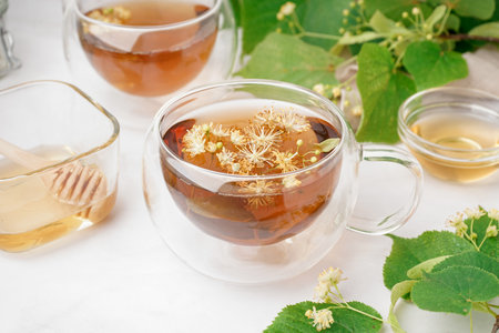 Glass cups of linden tea and bowls with honey on white backgroundの写真素材