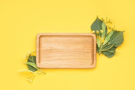 Composition with wooden board and fresh linden flowers on yellow background