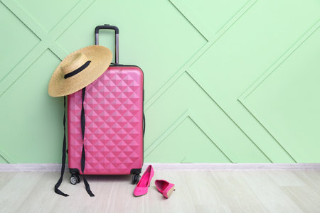 Suitcase with stylish wicker hat and high heels near green wall. travel conceptの写真素材