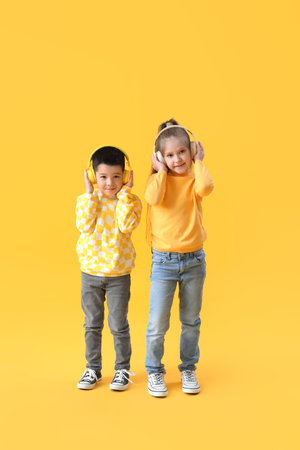 Cute little children in headphones and sweaters on yellow backgroundの写真素材