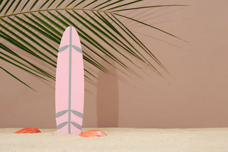 Mini surfboard with seashells and palm leaf on sand against brown backgroundの写真素材