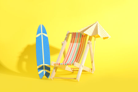 Creative composition with miniature surfboard, deck chair and umbrella on yellow backgroundの写真素材