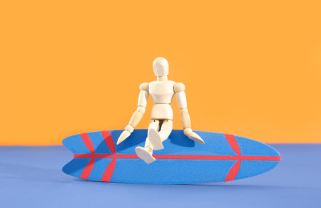 Mini surfboard with wooden mannequin on blue table against orange backgroundの写真素材