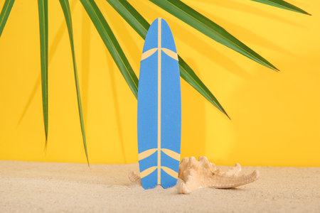 Mini surfboard with starfish and palm leaf on sand against yellow backgroundの写真素材