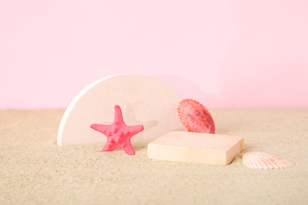 Decorative plaster podiums with seashells and starfish on sand against pink backgroundの写真素材