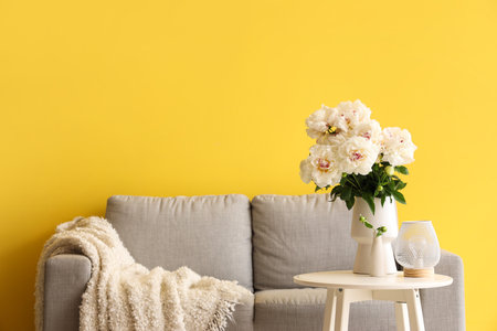 Vase of white peonies with coffee table and couch near yellow wallの写真素材