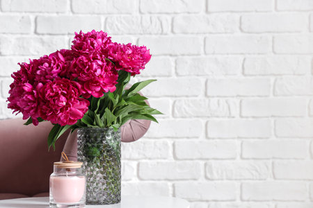 Vase of red peonies with candle on coffee table and couch near white brick wallの写真素材