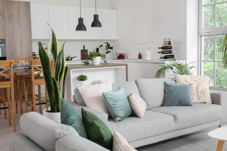 Interior of light open space kitchen with cozy gray sofas and island table