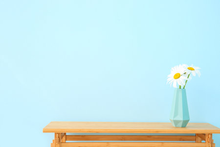 Wooden table with blooming daisy flowers in vase near blue wallの写真素材