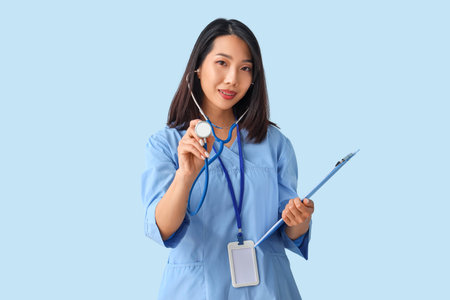 Female Asian medical intern with stethoscope and clipboard on blue backgroundの写真素材