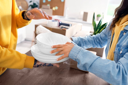 Young couple wrapping dishes with stretch film in kitchen on moving day, closeupの写真素材