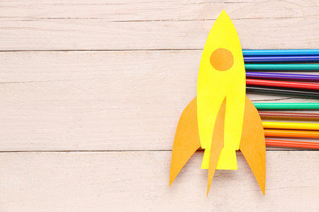 Yellow paper rocket with color pencils on beige wooden backgroundの写真素材