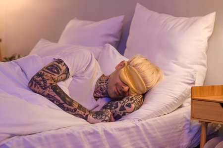 Young tattooed man sleeping in bed at nightの写真素材