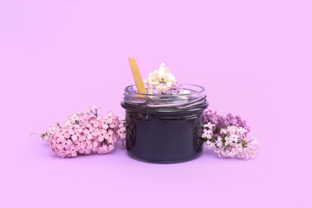 Jar of blueberry jam with wooden spoon and flowers on lilac backgroundの写真素材