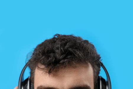 Young brunette man in headphones on blue background, closeupの写真素材