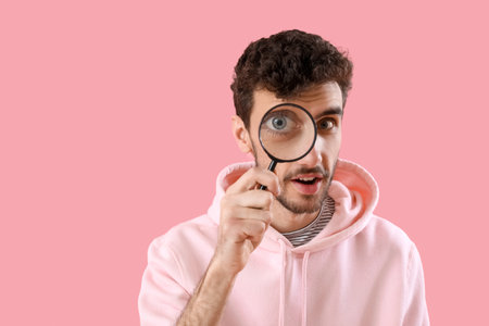 Young man with magnifier on pink background, closeupの写真素材
