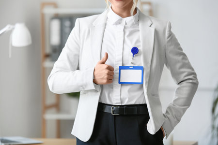 Young businesswoman with blank badge showing thumb-up in office, closeupの写真素材