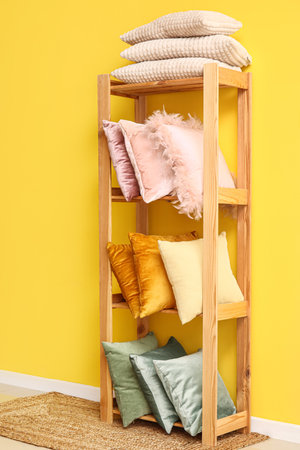 Shelving unit with stylish pillows near yellow wall in roomの写真素材