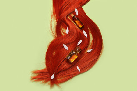 Composition with ginger hair strand, bottles of essential oil and flower petals on green background, closeupの写真素材