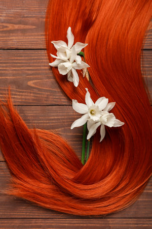 Ginger hair strand with beautiful narcissus flowers on wooden background, closeupの写真素材