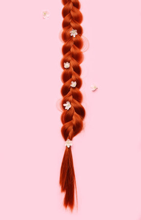 Braided ginger hair with flowers on color background, closeup