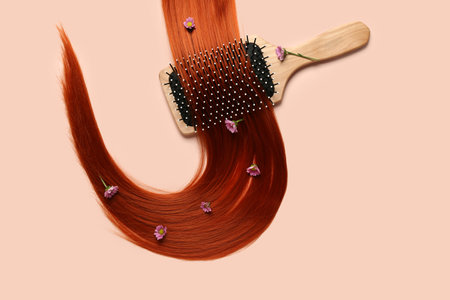 Composition with ginger hair strand, flowers and brush on color backgroundの写真素材