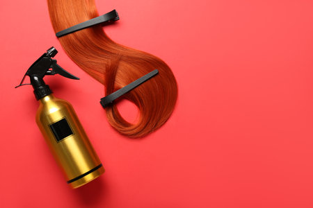 Ginger hair strand with clips and sprayer on red backgroundの写真素材