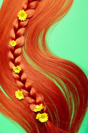 Ginger hair with braided strand and flowers on color background, closeupの写真素材