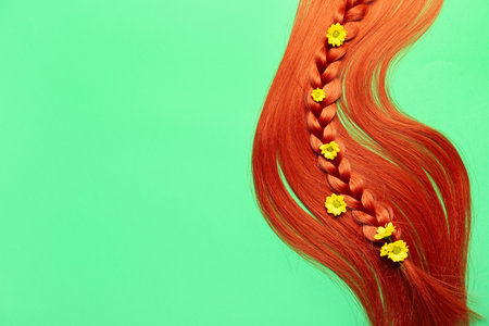 Ginger hair with braided strand and flowers on color backgroundの写真素材