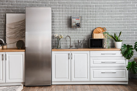 Interior of light kitchen with stylish fridge, counters, picture and houseplantsの写真素材