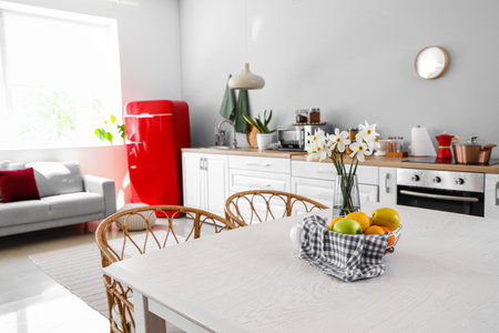 Basket with fruits and narcissus flowers on table in light kitchenの写真素材