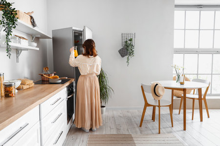 Young woman opening stylish fridge in kitchenの写真素材