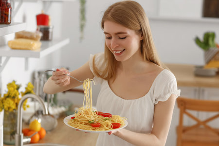 Young woman eating tasty pasta in the kitchenの写真素材