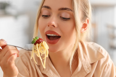 Young woman eating tasty pasta in kitchen, closeupの写真素材