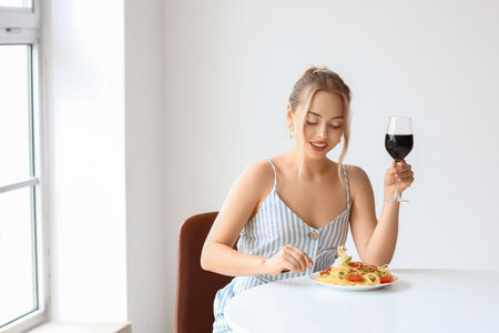 Young woman with tasty pasta and glass of wine sitting at table in restaurantの写真素材