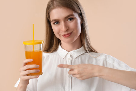 Young woman pointing at glass of carrot juice on beige background, closeupの写真素材