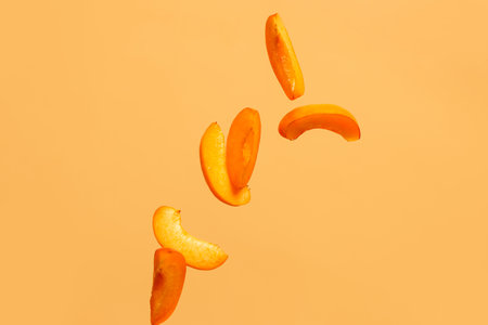 Flying pieces of fresh apricot on orange backgroundの写真素材