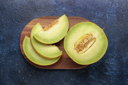 Wooden board with half of sweet melon and pieces on blue backgroundの写真素材