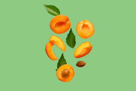 Flying halves of fresh apricot with pieces and leaves on green backgroundの写真素材